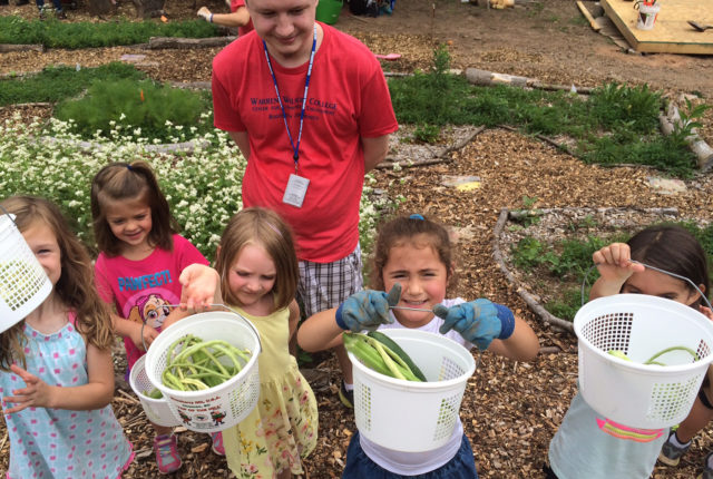 Children hold up buckets of vegetables they picked in the garden