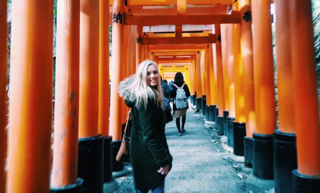 A student on a study away trip to Japan standing under Torri gates