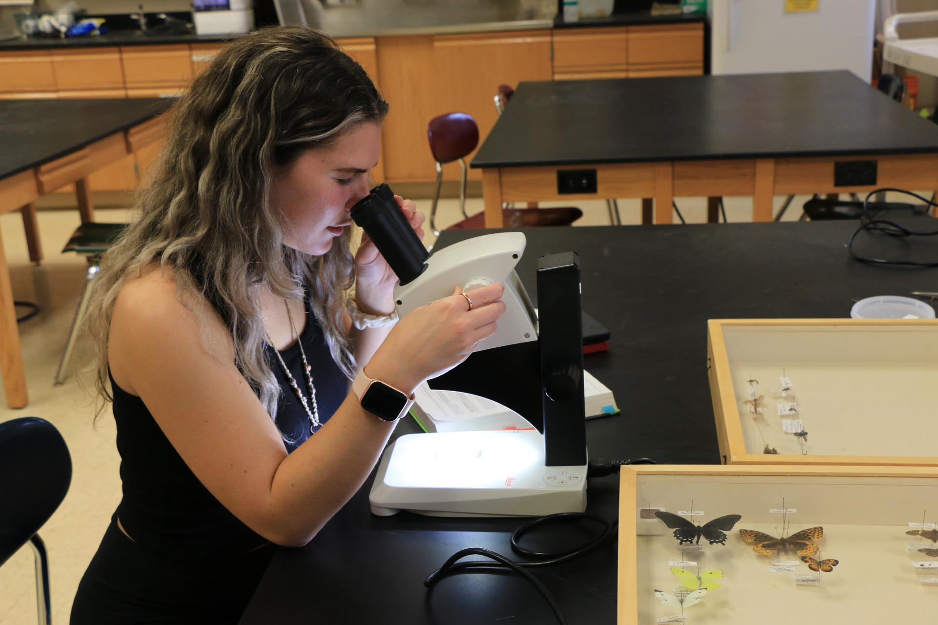 A biology and environmental studies crew student studies a sample through a microscope