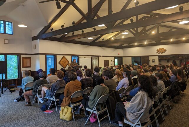 A large group of students gather for a creative writing event. They are seating facing a single speaker.