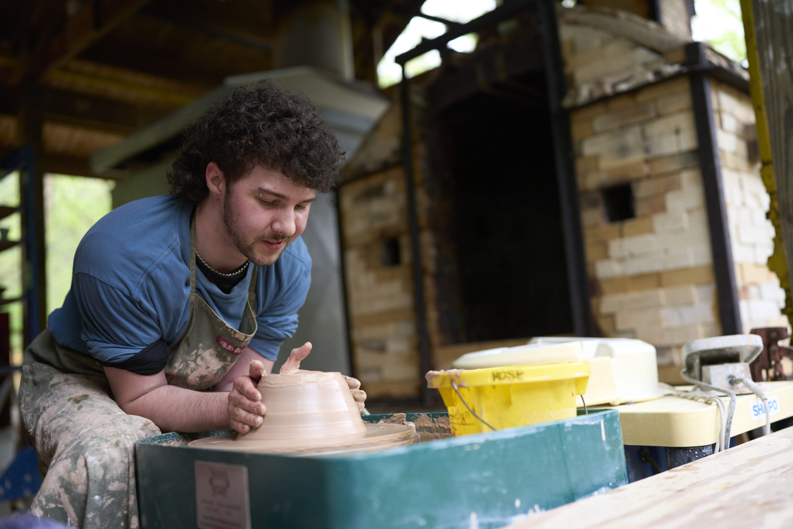 Ceramics student runs a pottery wheel in the outside 3d art space during a craft fair.