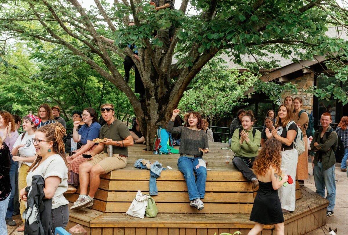 A group of students sit on the tree benches in front of the cafeteria waiting for the parade to pass by