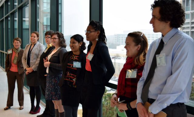 Students stand in front of a window wearing formal clothes