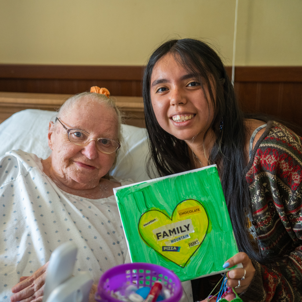 Alum Monica sits with an elderly patient holding a painting she helped her make.
