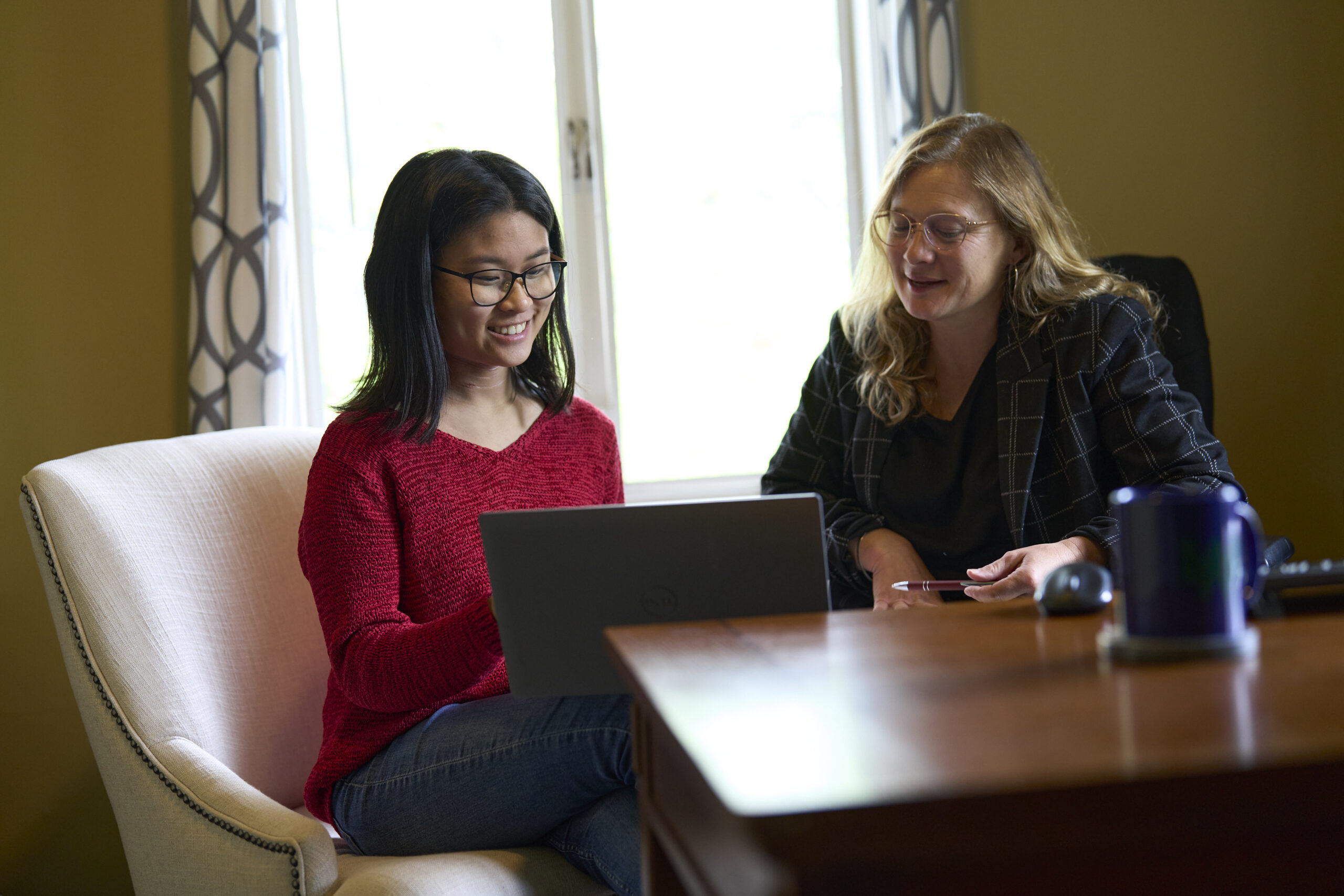 Sophia Huang works with Amy Ager on a project at the computer. They are smiling and speaking with one another.