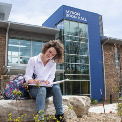 Student writes outside Myron Boon Hall