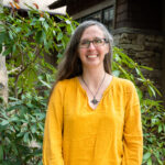 Faculty Member Charlotte Taylor stands smiling outside of Orr Cottage.