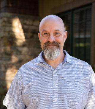 Faculty Member Jack Ingelman stands smiling outside of Orr Cottage.