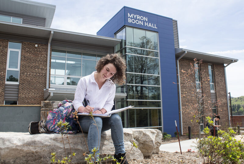 A student studying in front of Myron Boon Hall