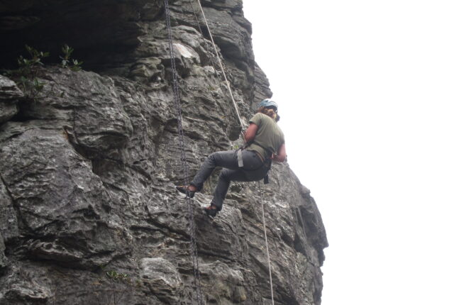 A student halfway up a cliff rock climbing.