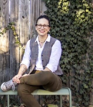 Alysia Sawchyn sits smiling in front of a fence covered in Ivy.