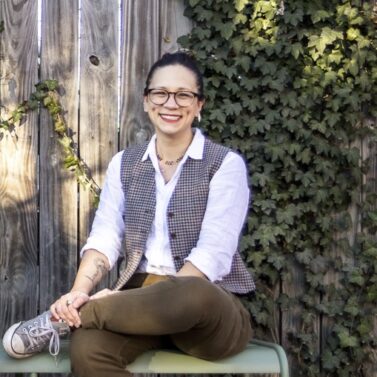 Alysia Sawchyn sits smiling in front of a fence covered in Ivy.