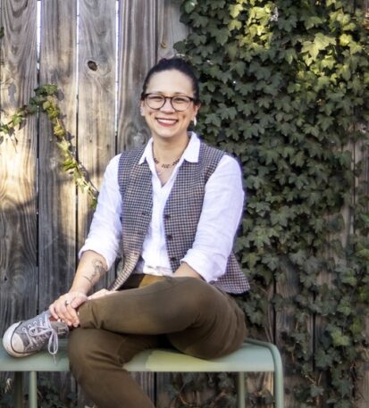 Alysia Sawchyn sits smiling in front of a fence covered in Ivy.