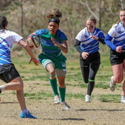 Four people are running in a rugby game. Three members of the opposing team are surrounding the one Warren Wilson Team member holding the ball.