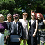 A graduate stands smiling with a group of their friends and family.