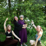 A Graduate hugs their older family member from behind and they hold a bouquet of flowers together. Two others hold their arms as though they are presenting the grad.