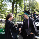 Anna Welton, holding a tree, shakes the hand of a graduate.