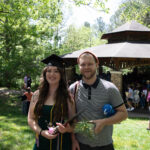 A grad stands with another person smiling