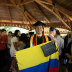 A grad holds their degree and a Columbian flag smiling.