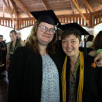 Two graduates stand smiling holding strawberries.