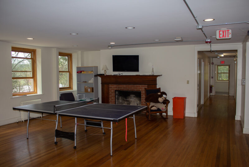 The common area in Sage Dorm. A pingpong table is in the middle of the room. A flat screen tv is mounted above a fireplace.