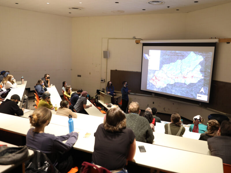 A student is presenting a map to a room full of people in Jensen Lecture Hall.