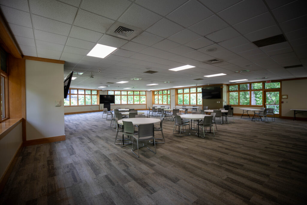 Canon Lounge is a large room with three televisions. There are 7 round tables and 3 long tables each surrounded by chairs.