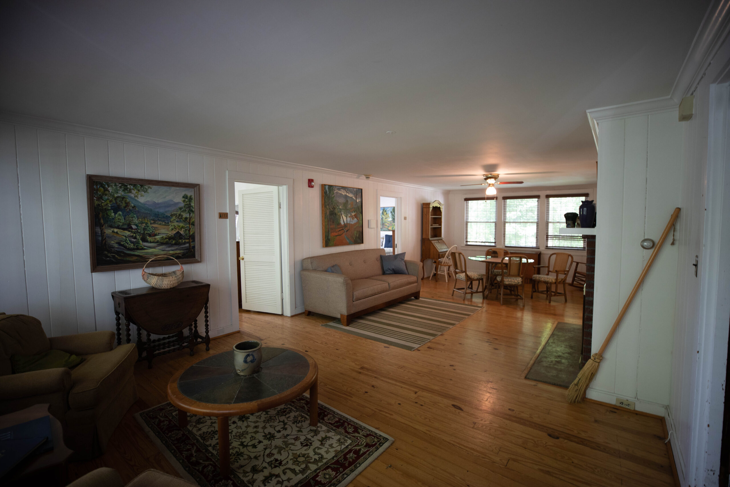 The living room of Apartment 1 in the St. Clair Guest House. Closest to the camera is a small sitting area with two chairs and a coffee table. In the middle of the room is a couch facing a fireplace. On the opposite side of the room there is a dining table with 4 chairs.