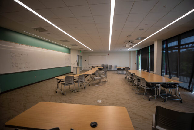 A conference room in Boon. Tables are arranged in different patterns around the room. There is a projector facing a large whiteboard that spans nearly the entire room.