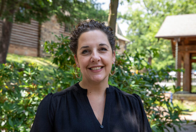 Vice President for Institutional Advancement, Marketing and Strategic Communications stands in front of Orr Cottage smiling.