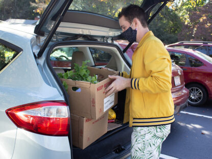 A masked student loads food into a car