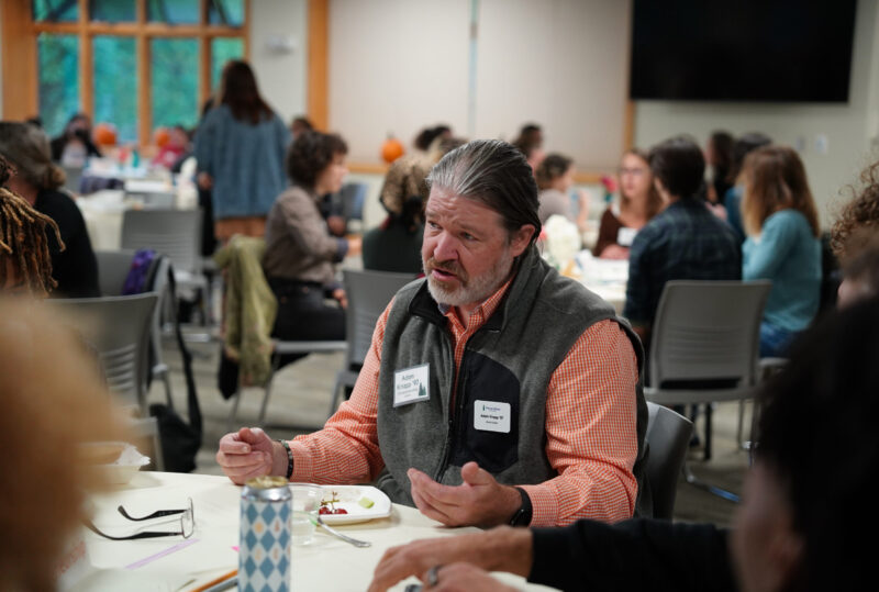 An alum sits at a table and talks to a group of students at a networking event