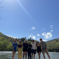 Students stand together in front of a lake on a beach.