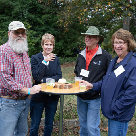 A group of four alumni stand around a table with beers and snacks