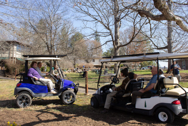 Students and faculty sitting in solar golf carts talk to one another.