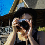 A student with a camera stands in front of the garden cabin