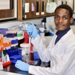 A student working in a lab wearing a lab coat and gloves.