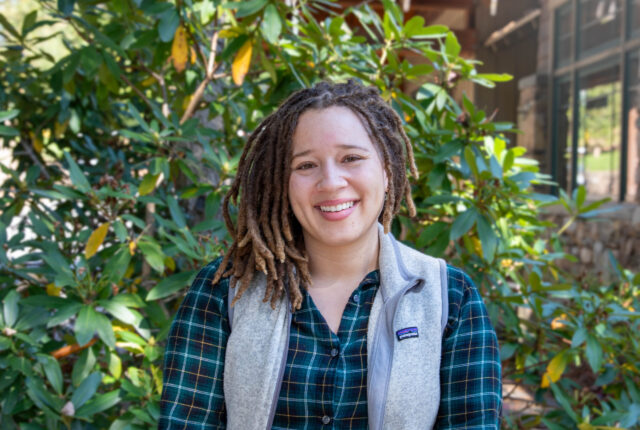 Admissions Counselor Sarah Farrar stands smiling in front of Orr Cottage