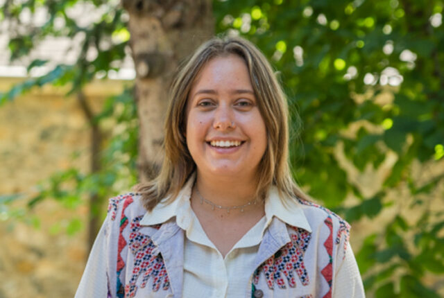 Admissions Counselor Holland Mueller stands smiling wearing a white top.