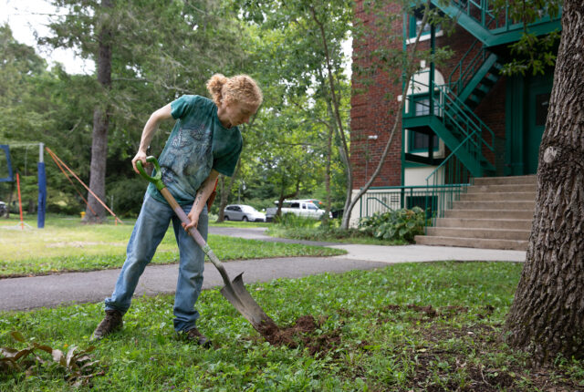 An ecological landscaping crew student shovels dirt in front of sunderland hall.