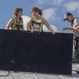 Students install a solar panel on the roof of the electric tractor barn.