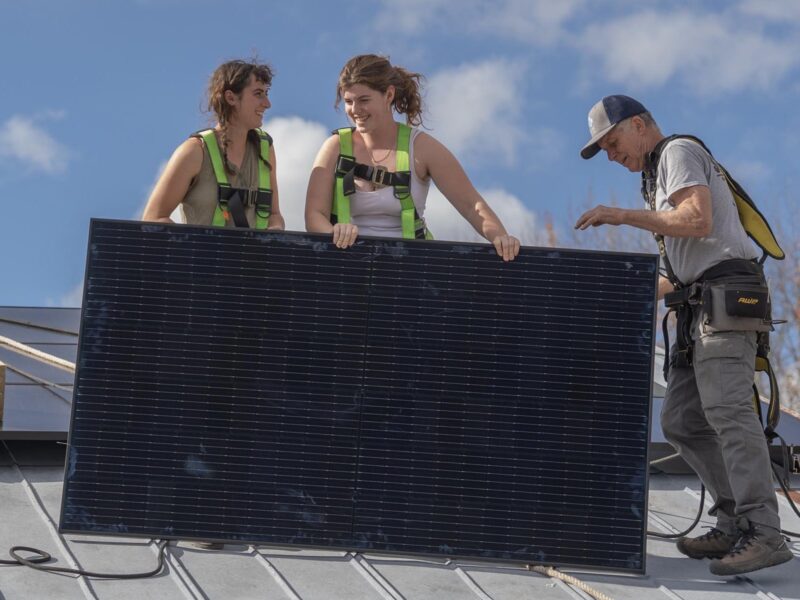 Students install a solar panel on the roof of the electric tractor barn.