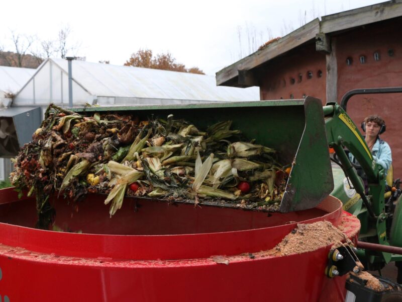 A student uses a tractor to scoop food waste into a compost bin