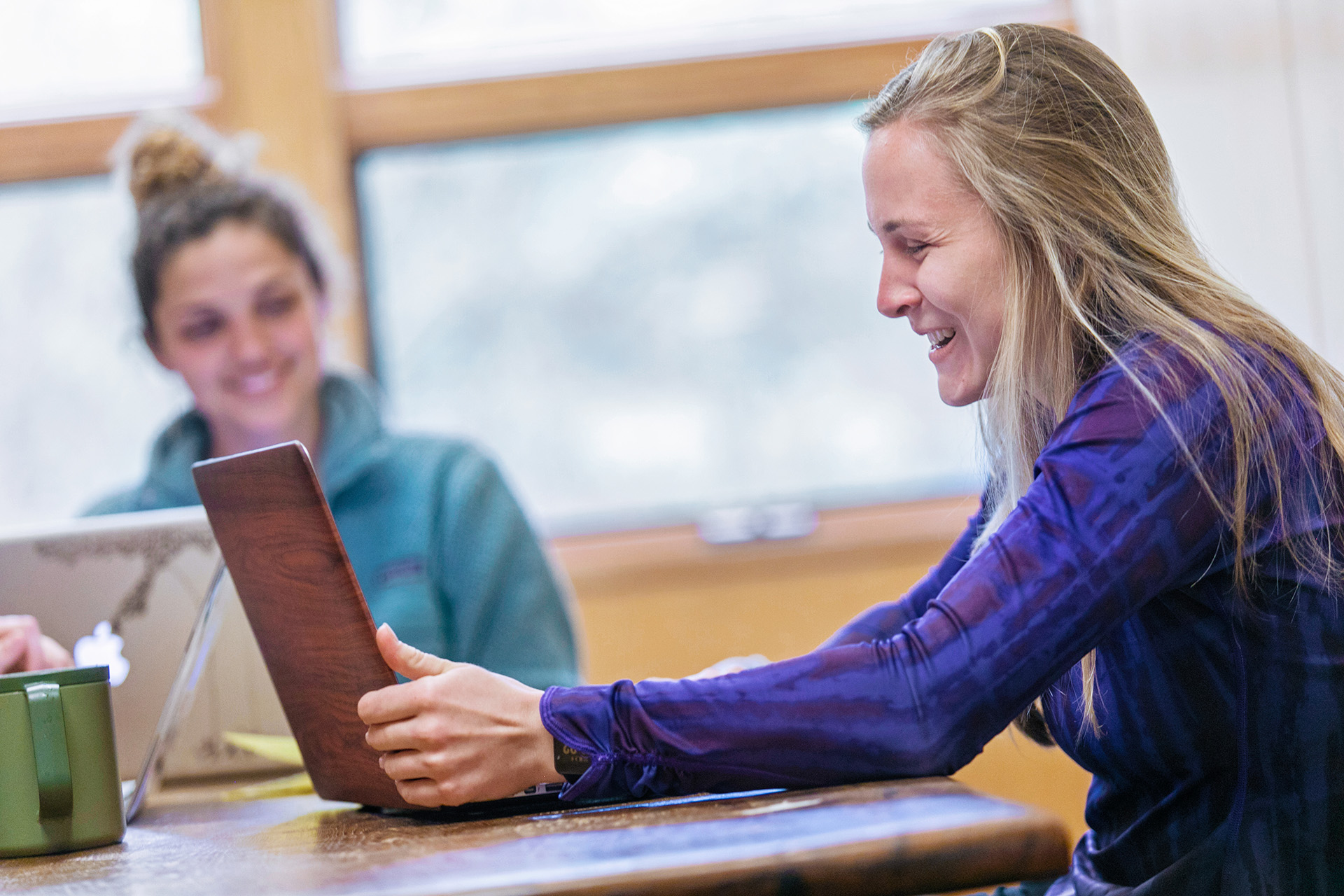 Two students sit beside each other looking at their laptops smiling