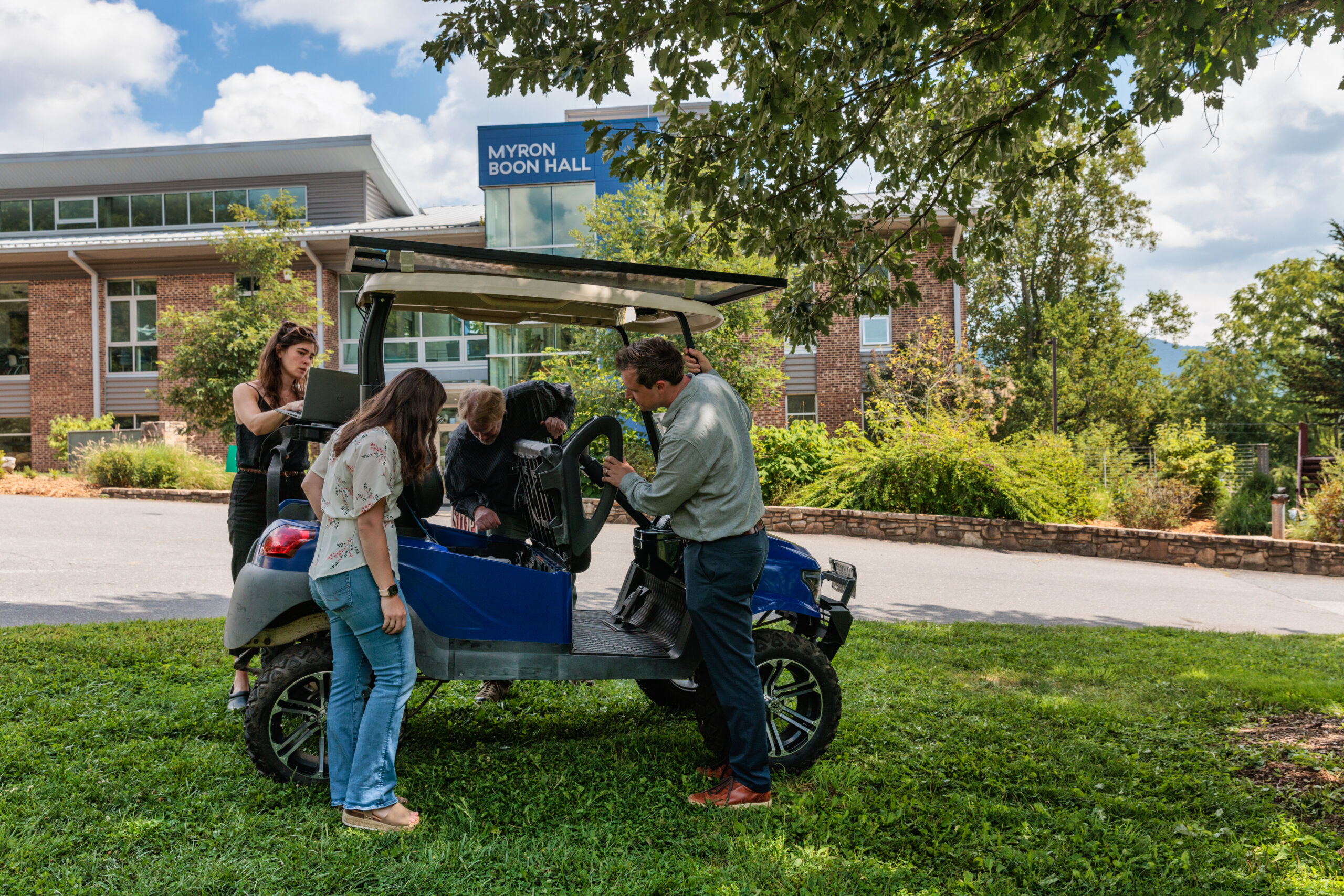 MACS students stand around and inspect the solar powered golf cart on campus.
