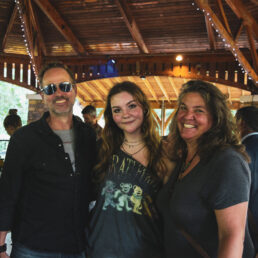 A student stands in the pavillion with their parents on either side. All three are smiling.