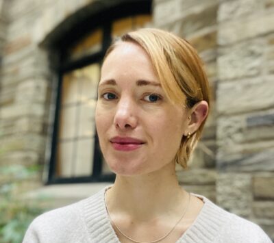 Assistant Director of the MACS program, Delilah Griswold, smiles in front of a stone wall.