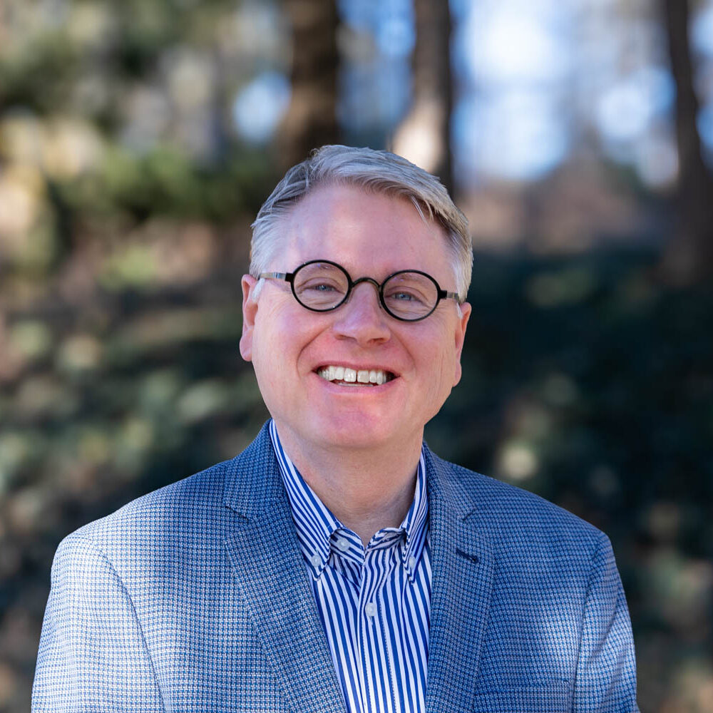 David Gliem stands in front of foliage and smiles for a headshot.