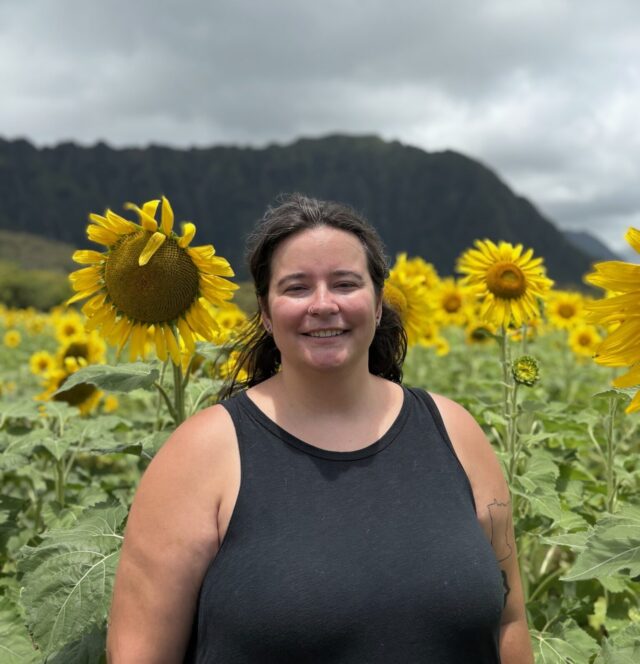Dr. Hannah Pearson stands and smiles in a sunflower field.
