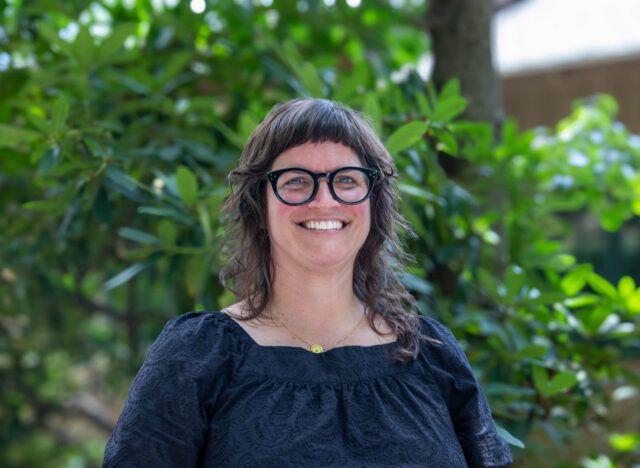 Director of the Library, Julia Haverstock stands and smiles in front of the admissions building at Warren Wilson College.
